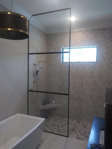 Frameless walk in shower door without handles and black matte finish. Walk in shower covers half of the shower wall with a tile wall and floor.