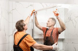 shower door installation by two men in overalls and orange shirt